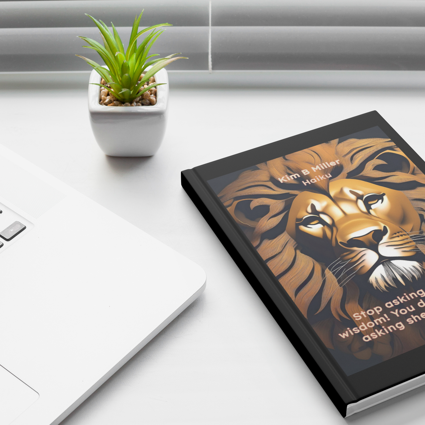 Hardcover Journal with a lion and haiku on wisdom written by Kim B Miller, partial view near laptop.