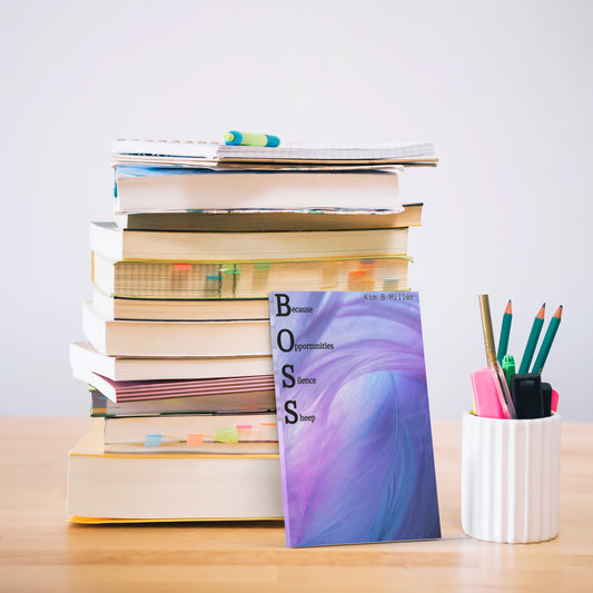 A stack of purple and blue custom sticky notes featuring the acronym “BOSS”, created by Kim B Miller, near books.